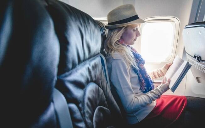 Mulher lendo um livro enquanto viaja sozinha de avião