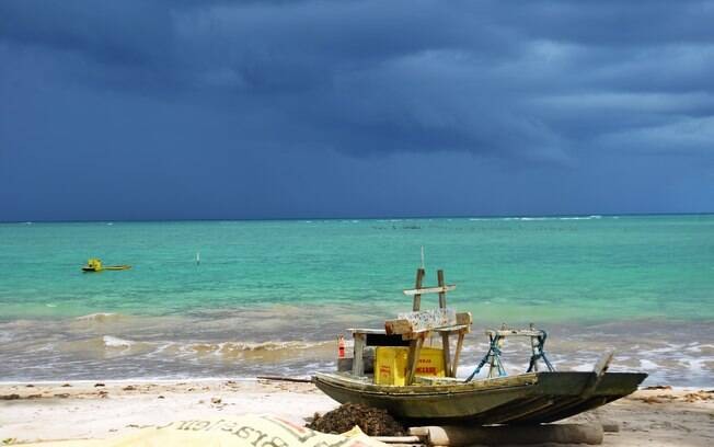 Praia com um barco na areia e mar azul claro.